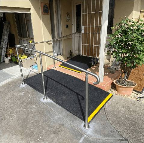 Wheelchair ramp with handrails Rubber wheelchair ramp with stainless steel handrails and yellow nosing at a front step